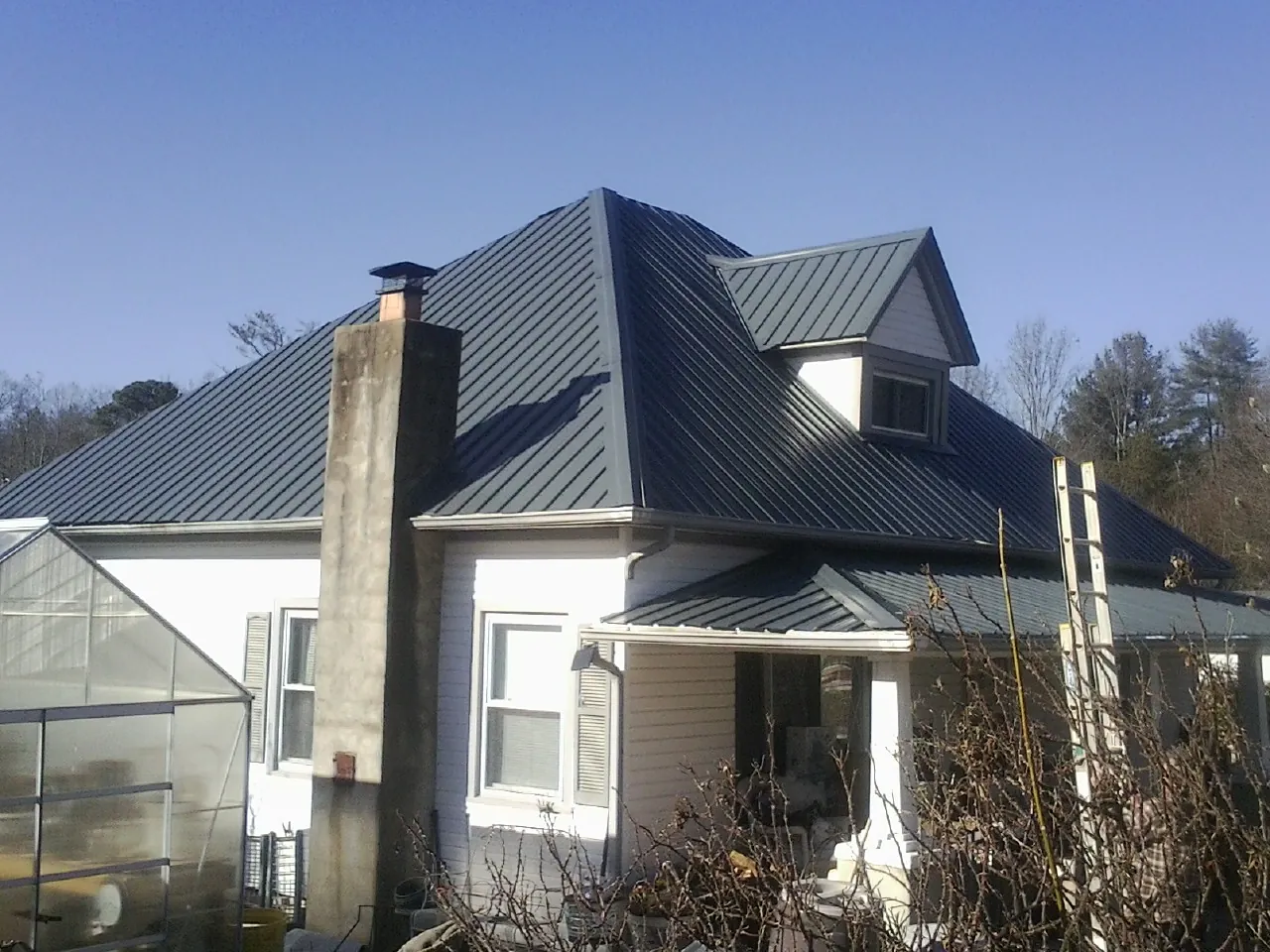Dark blue standing seam metal roof on a white farmhouse with dormer in Bickleton