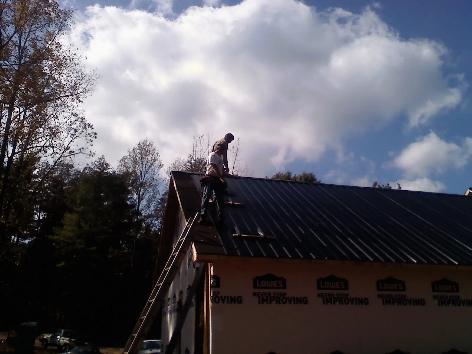 Roofer fastening dark metal panels high against a cloudy sky, from a Roof Inspection job in Bickleton